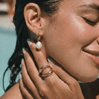 Mujer con pendientes de argolla dorados y perla blanca colgante