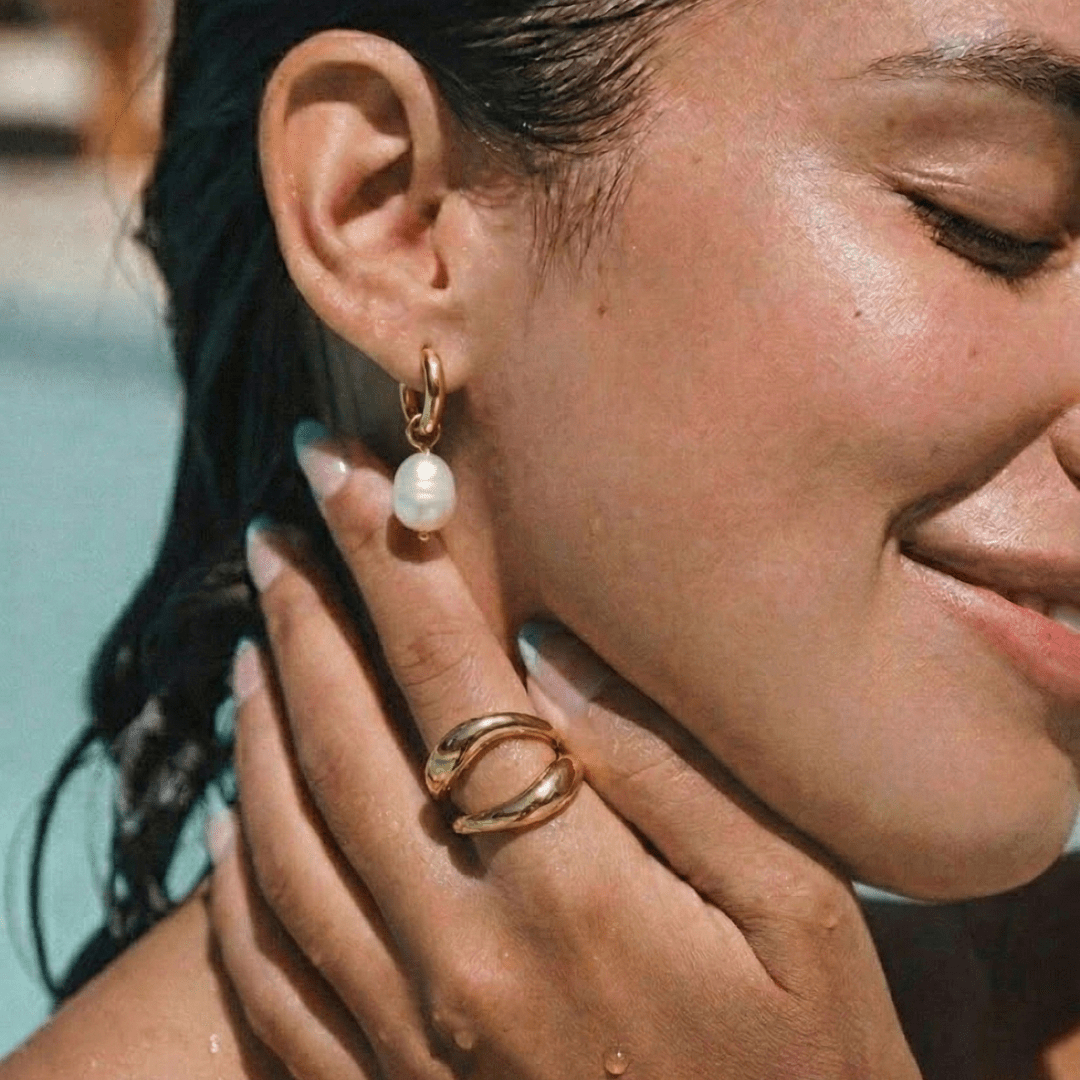 Mujer con pendientes de argolla dorados y perla blanca colgante