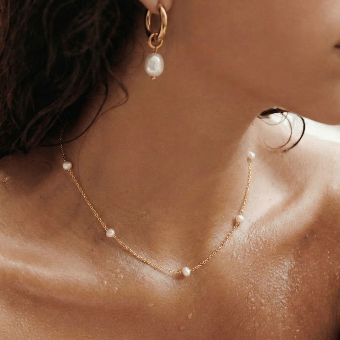Aros dorados con perla blanca; detalle en el cuello y la oreja
