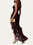 Vestido elegante negro con estampado floral rojo, volantes en capas y abertura; perfil trasero.