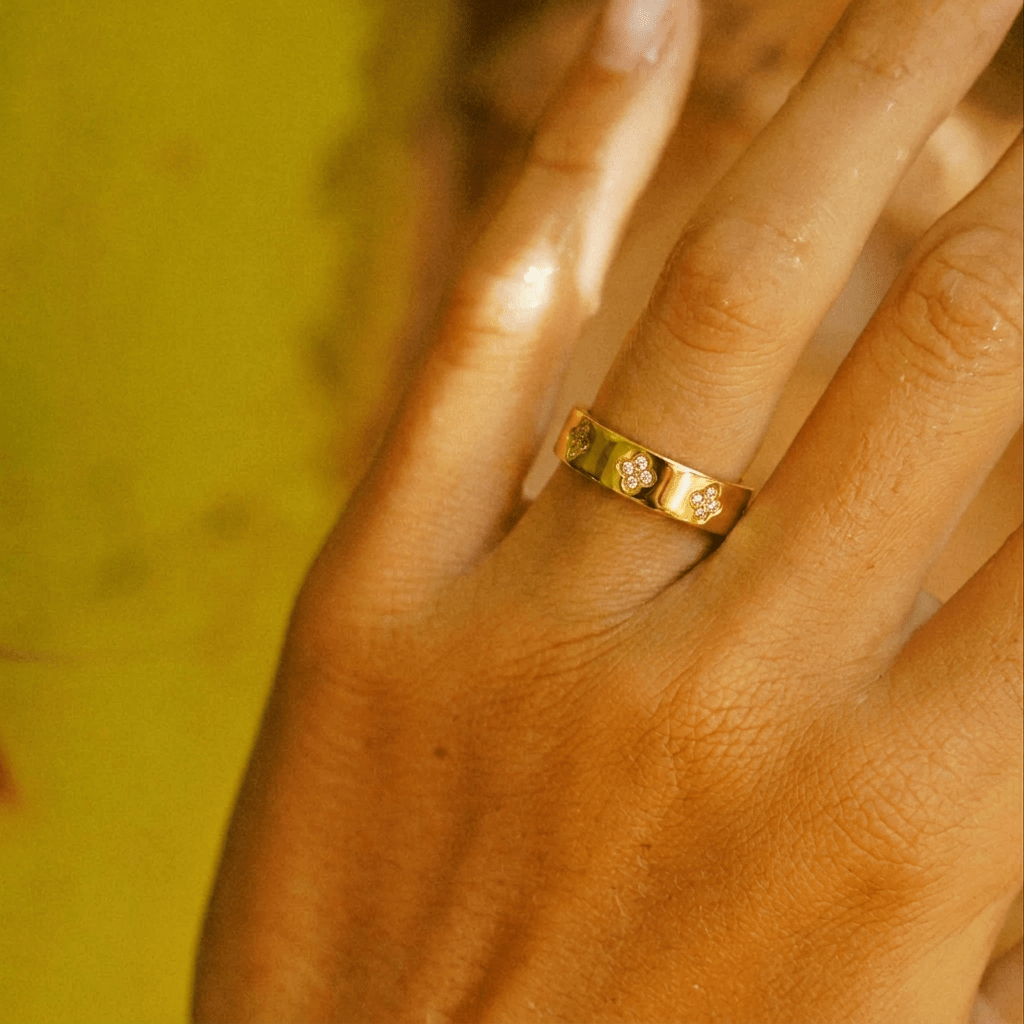 Anillo dorado con trébol central y pequeñas piedras brillantes en la banda