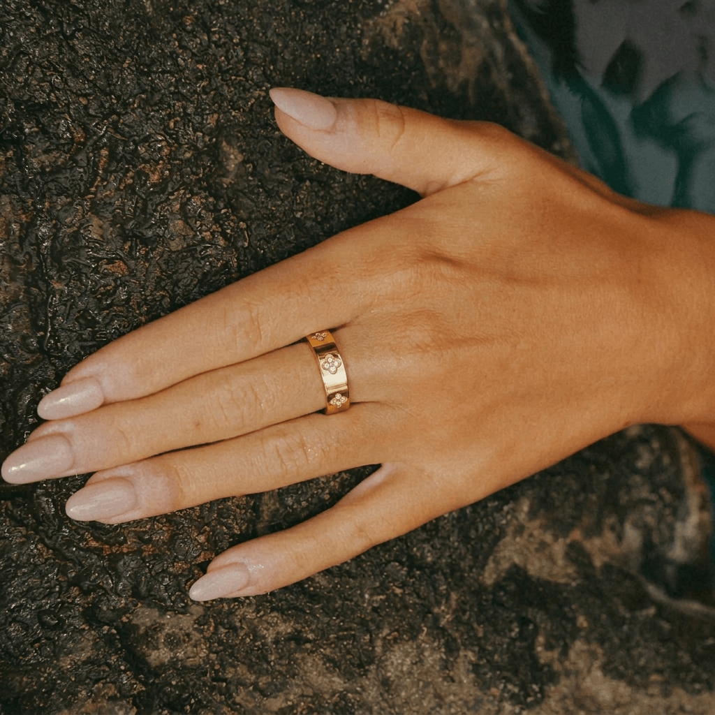 Anillo dorado con tréboles y piedras brillantes sobre la mano