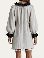 Minivestido beige con borlas en el bajo, volante negro en el escote y mangas abullonadas