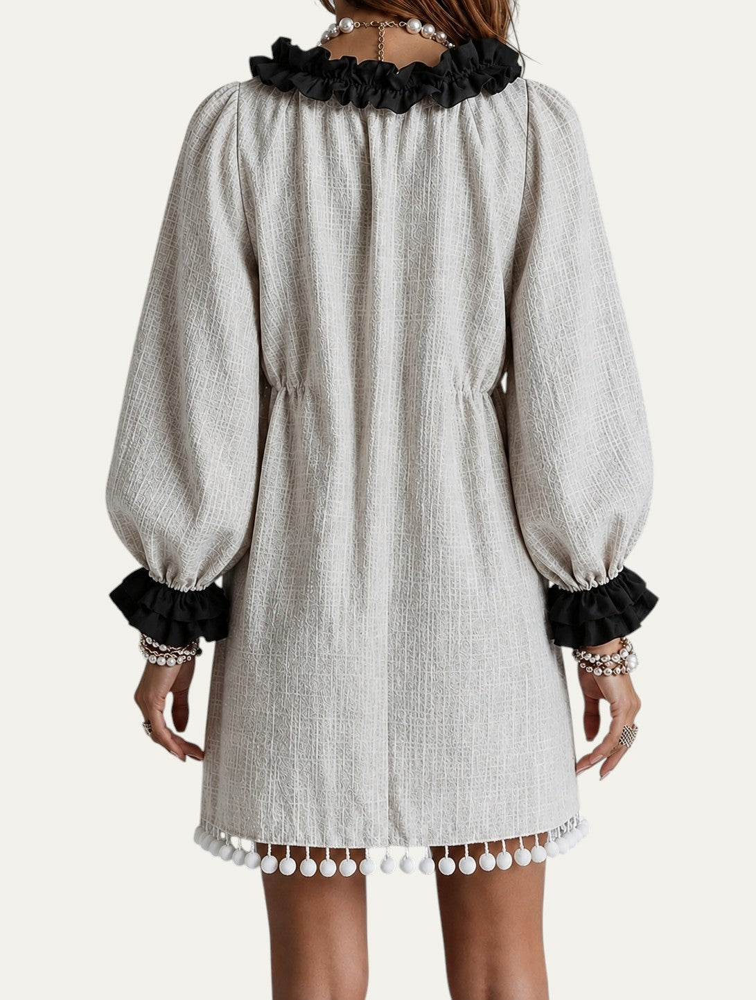 Minivestido beige con borlas en el bajo, volante negro en el escote y mangas abullonadas