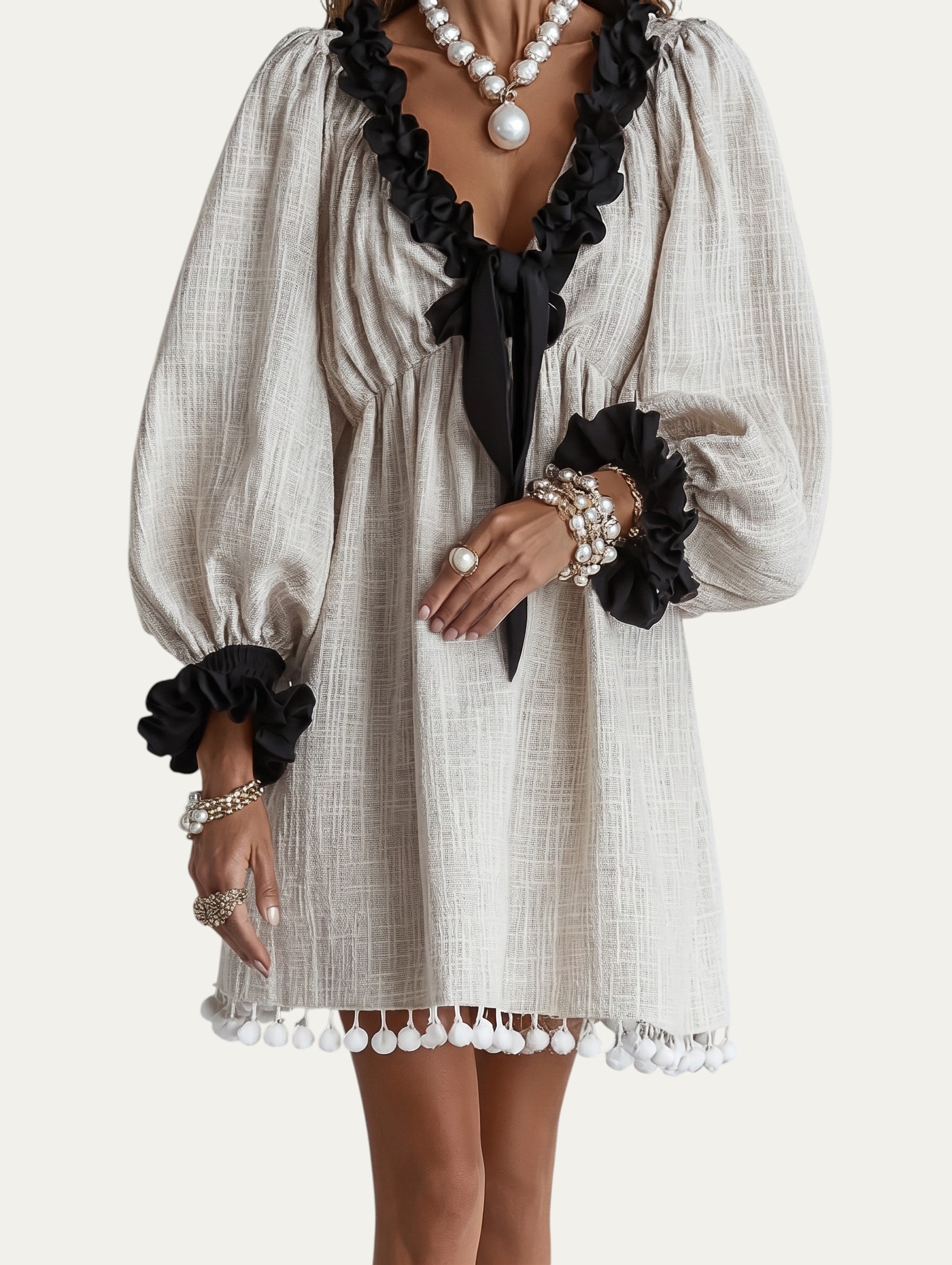 Minivestido beige con bordes ondulados negros, mangas abullonadas y borlas en el bajo